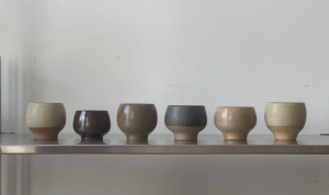 Six handmade ceramic cups arranged on a shelf.